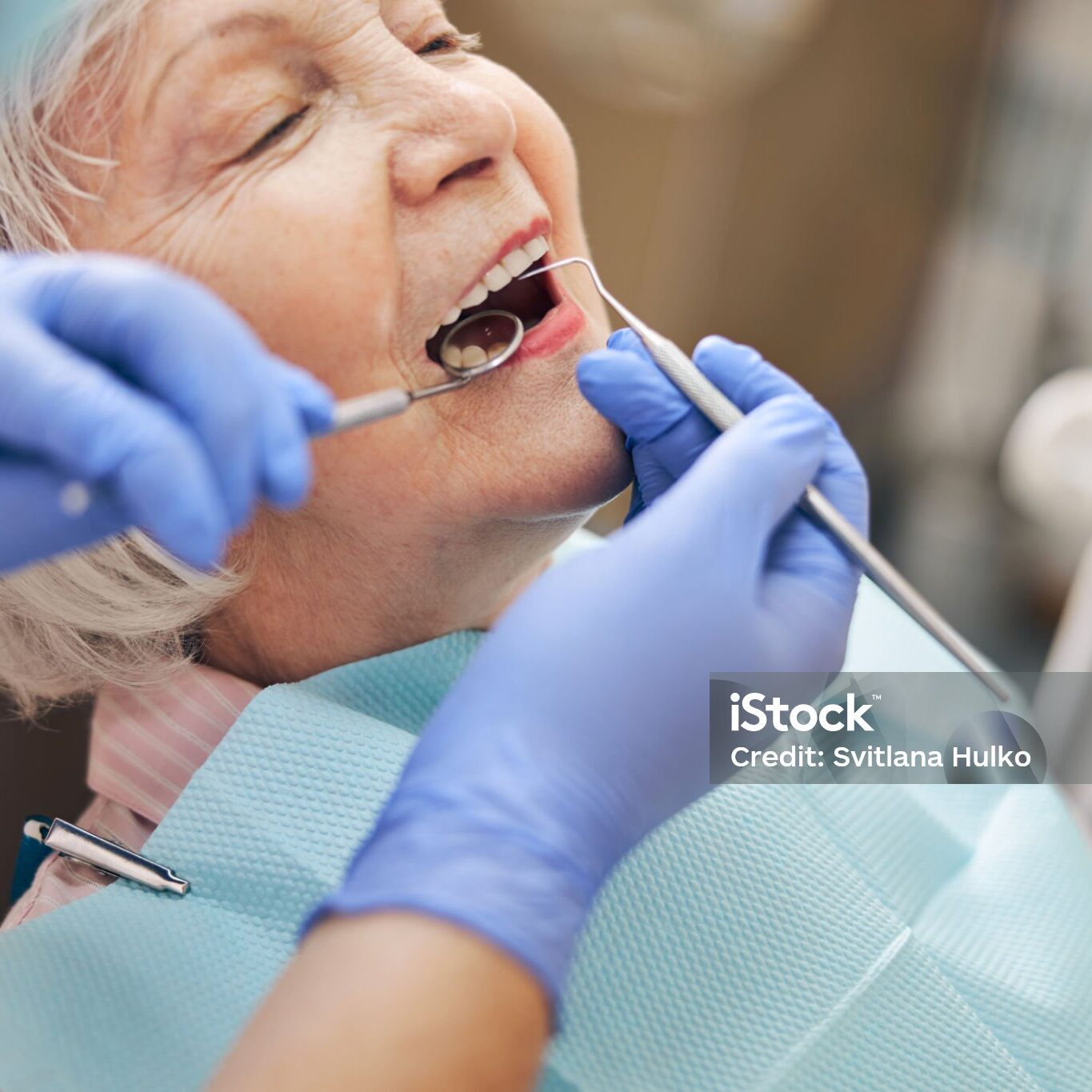 Female dentist examining teeth of adult charming missis with mouth mirror and probe checking